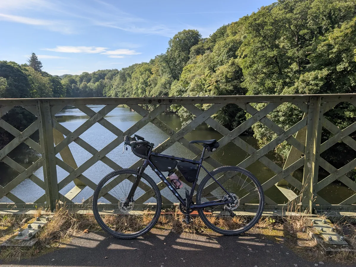 A bike on an iron bridge over a wooded river